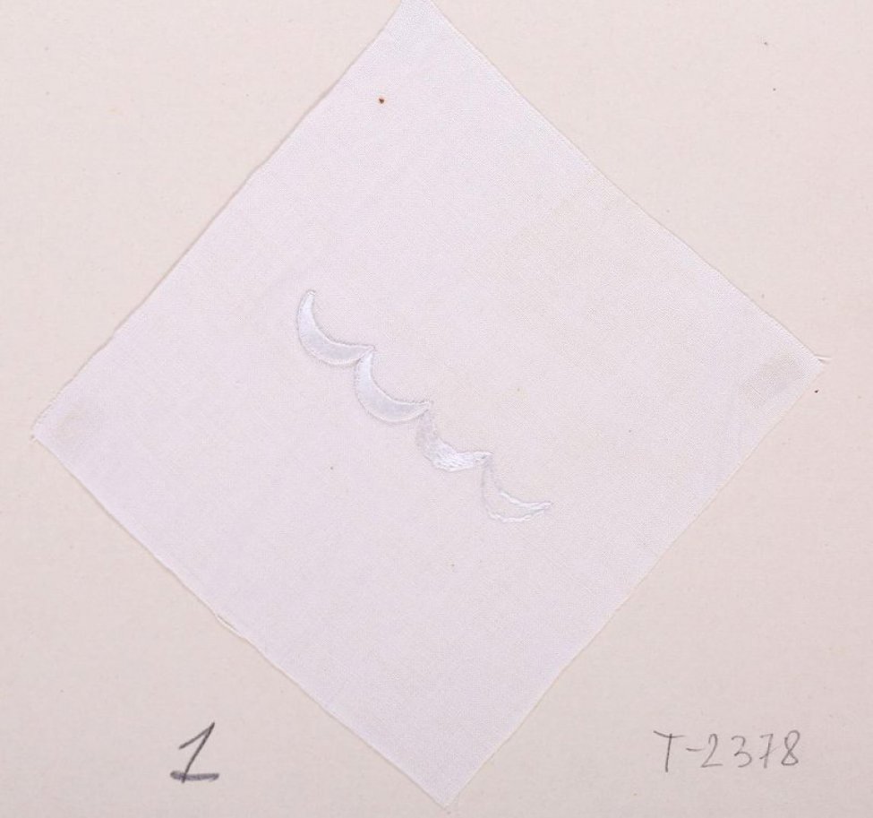 На белом батисте квадратной формы в центре дан образец последовательности выполнения шитья гладью. Образец в виде четырех фестонов. Образец одним углом приклеен к картонному листу.