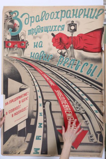 Изображена на верху красная рука, переводящая стрелку. Слева виден паровоз идущего поезда. Между рельсами красная стрелка с надписью: