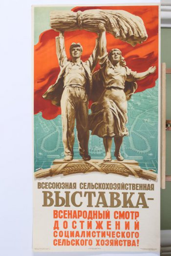 Изображены мужчина и женщина со снопами над головой.На фоне -план выставки и вверху- красное знамя.