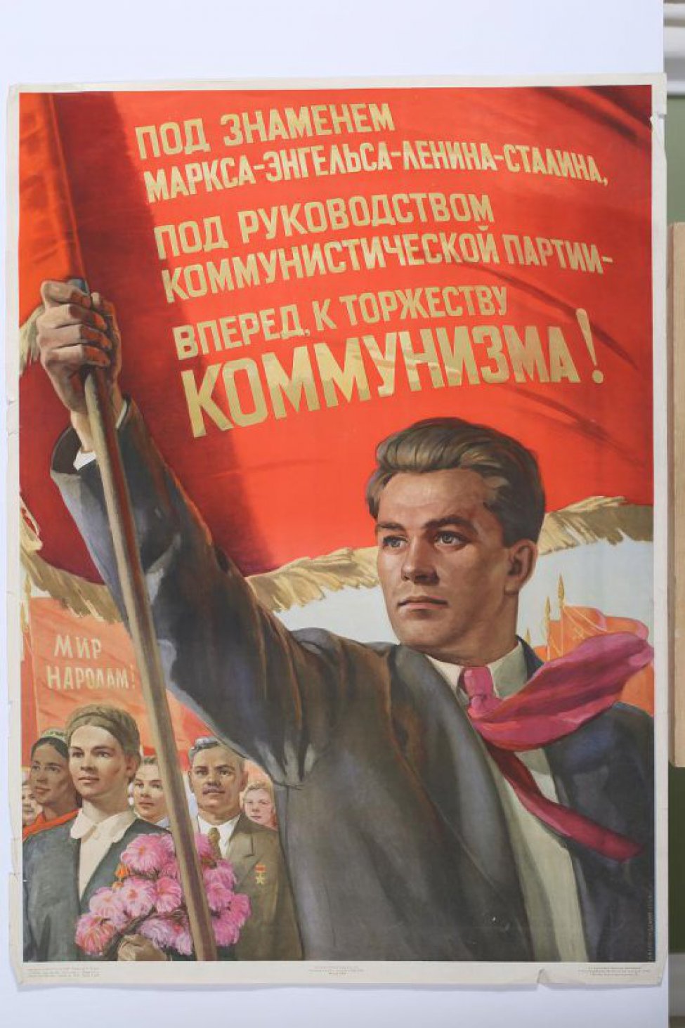 Изображен молодой мужчина погрудно в алом галстуке с красным знаменем в правой руке.На знамени текст. Справа от него мужчины и женщины с цветами и знаменами.Справа внизу сбоку: " Б.Белопольский 1954г."