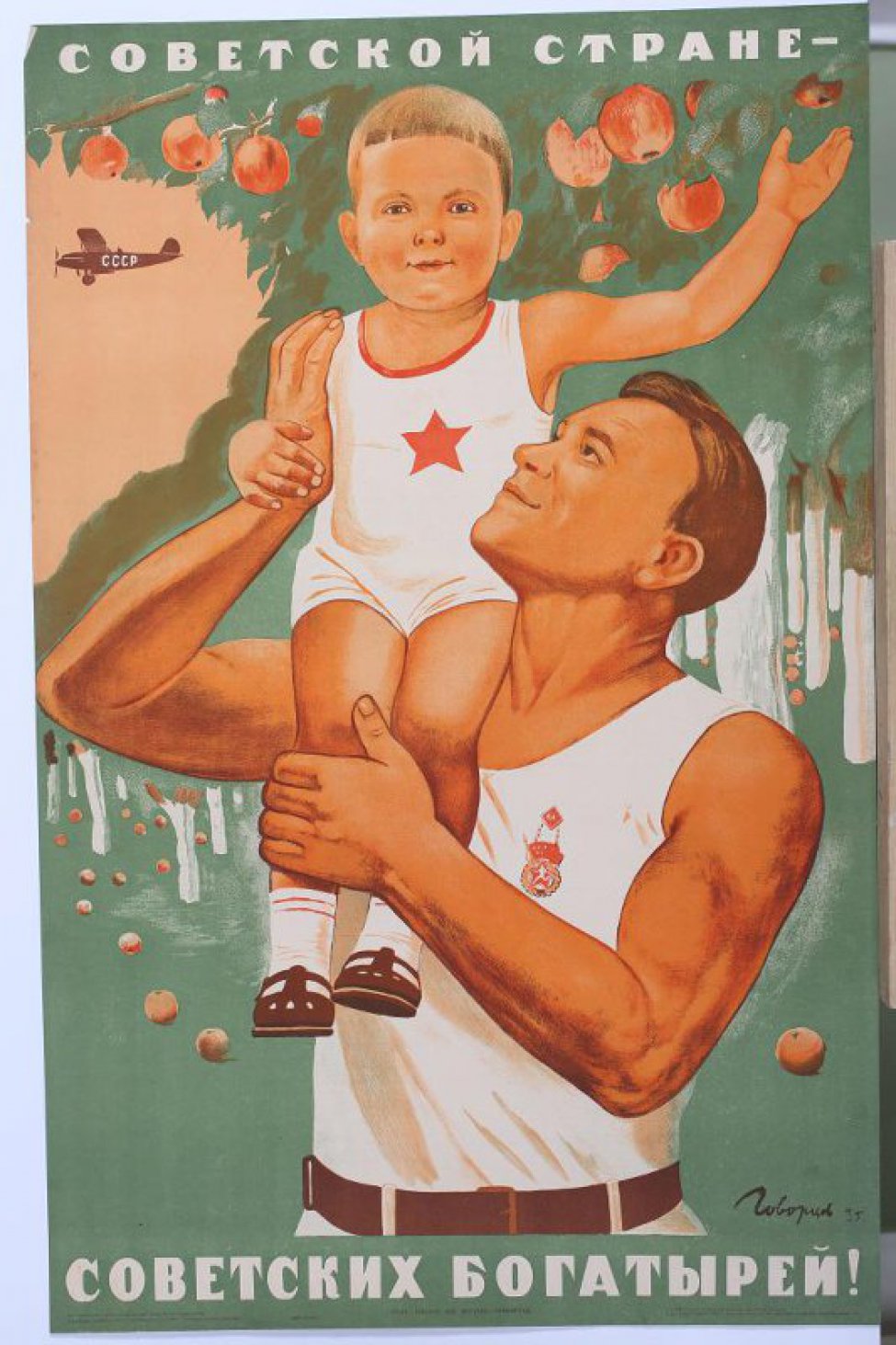 Изображен здоровый молодой мужчина в белой майке. На плече держит здорового красивого ребенка тоже в майке со звездой на груди.