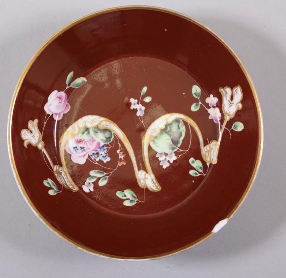 Блюдце чайное коричневое. На зеркале роспись: цветы и золоченый фигурный орнамент. Край блюдца позолочен.
