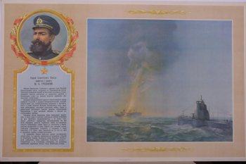 Изображено: Слева в венке портрет Героя Советского Союза капитана 1 ранга  М.В.Грешилова. Справа- море, подводная лодка и горящий корабль.