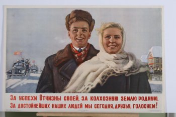 Изображены погрудно молодой парень в зимней шапке и девушка в белой шали. Справа от них едут на грузовиках с красными знаменами мужчины и женщины, слева- избирательный участок. Под изображением текст. Слева внизу: 