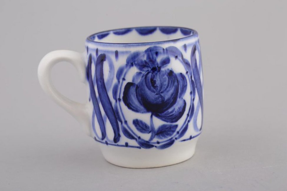 чашка белая, цилиндрической формы, сужающаяся к верху.  По тулову стилизованное изображение роз в волнообразном  обрамлении и спиралевидный орнамент.