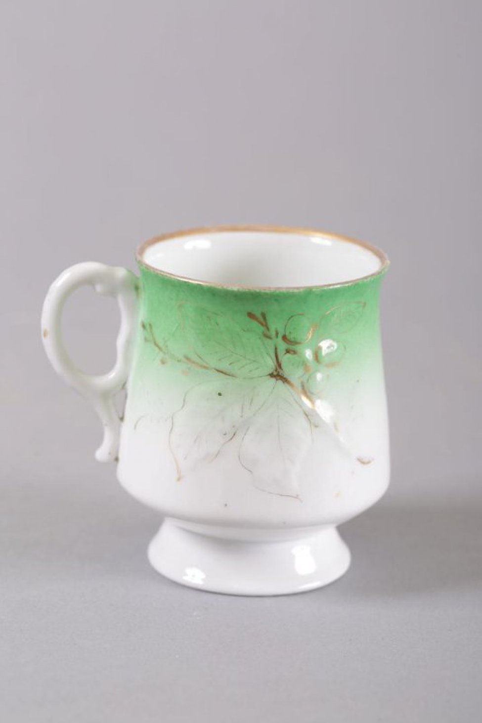 Чашка белая, внизу тулова с постепенным переходом в зеленый цвет. На тулове рельефное изображение виноградной ветки с надглазурной позолотой.