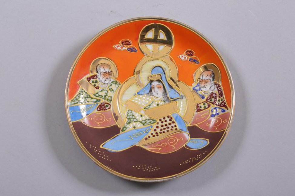 Блюдце мелкое, на низкой кольцевой ножке. На зеркале и по борту - композиция из трех фигур (двух мужчин и одной женщины в центре), одетых в "восточные" одежды. Фон в верху - оранжевый, внизу - коричневый.