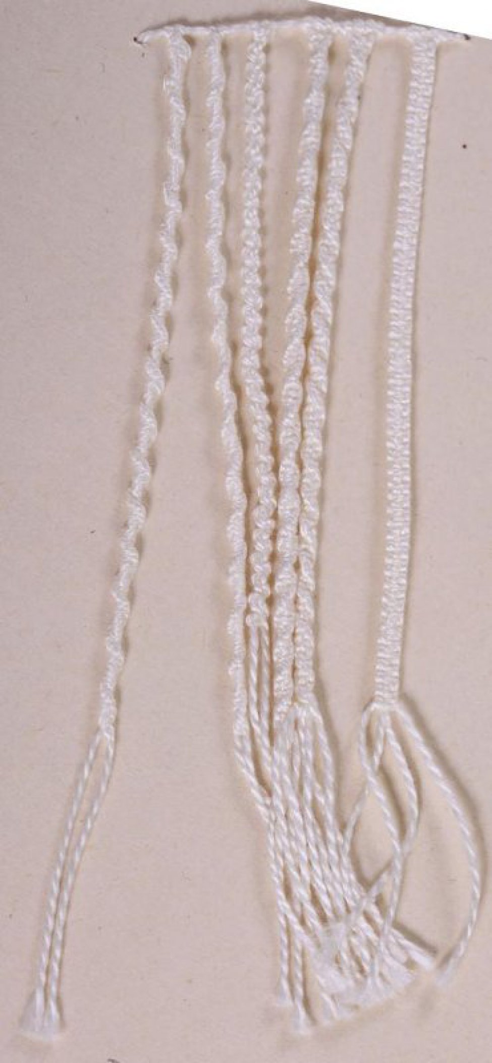 Шесть шнуров простого плетения соединены в верхней части. На концах каждого шнура бахрома. 3 шнура из двух нитей. 3 шнура из четырёх нитей. Образец пришит к картонному листу.