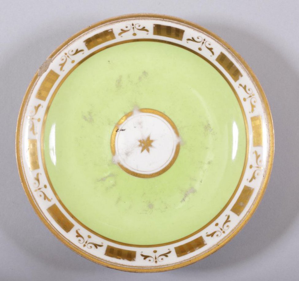 Блюдце чайное светло-зеленое. По краю борта - золоченый орнамент. На зеркале - круглый белый медальон с золоченым ободком и золоченой звездочкой в центре.