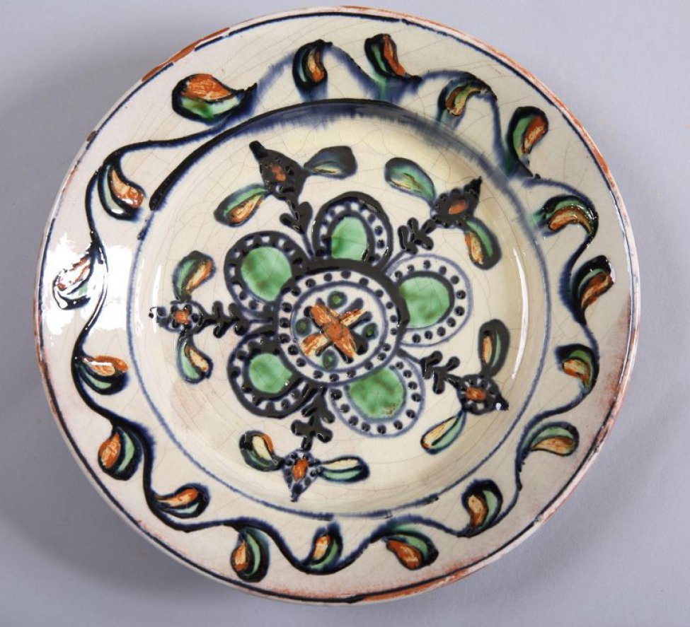 Тарелка серовато-белая, орнаментирована узорами синего, зеленого и желто-коричневого цвета.  Обратная сторона - красно-охристого цвета, покрыта глазурью.