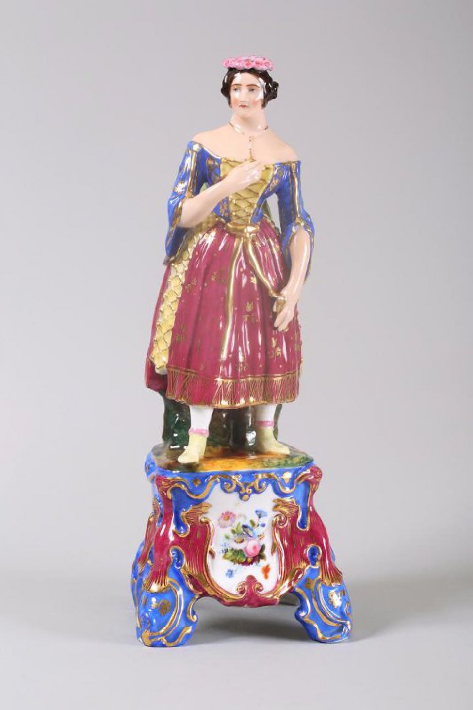 На высоком постаменте изображена стоящая женщина с прижатой к груди рукой,  в испанском костюме 50-х годов 19 века. На голове женщины венок с лентой; одета в синюю, с желтой вставкой,  блузку, и красную, с желтыми вставками, юбку.  На постаменте белый медальон с изображением цветов.