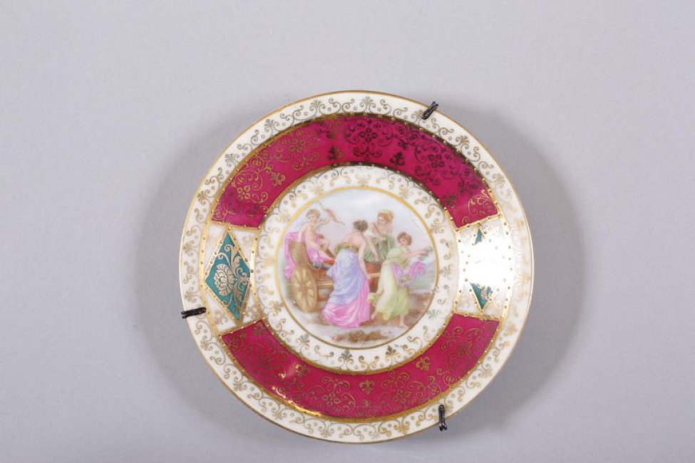 Блюдце с малиновым бортом и белым краем, с двумя медальонами на борте. На зеркале роспись: три женщины везут в колеснице амура.