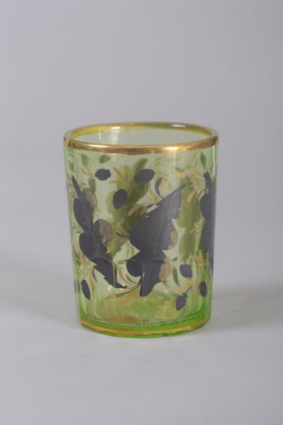 Стакан светло-зеленый, с гранями по низу тулова. По наружной стороне стакан расписан золотом и чернью крупными и мелкими листьями и мелкими цветочками.