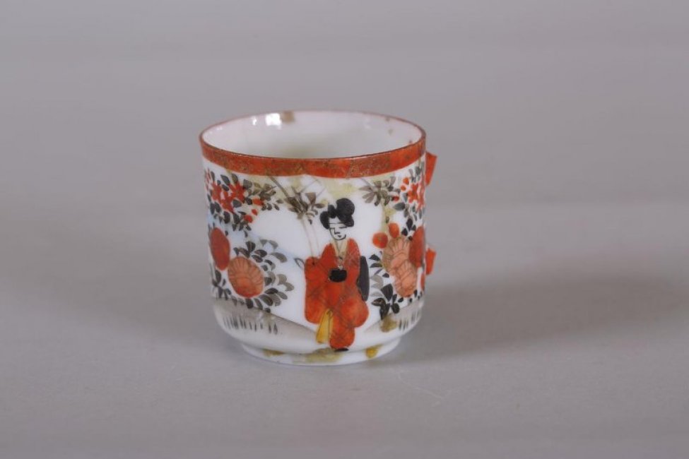 Чашка чайная, украшена изображением китаянок среди цветов и красно-золотистой каймой по краю борта.