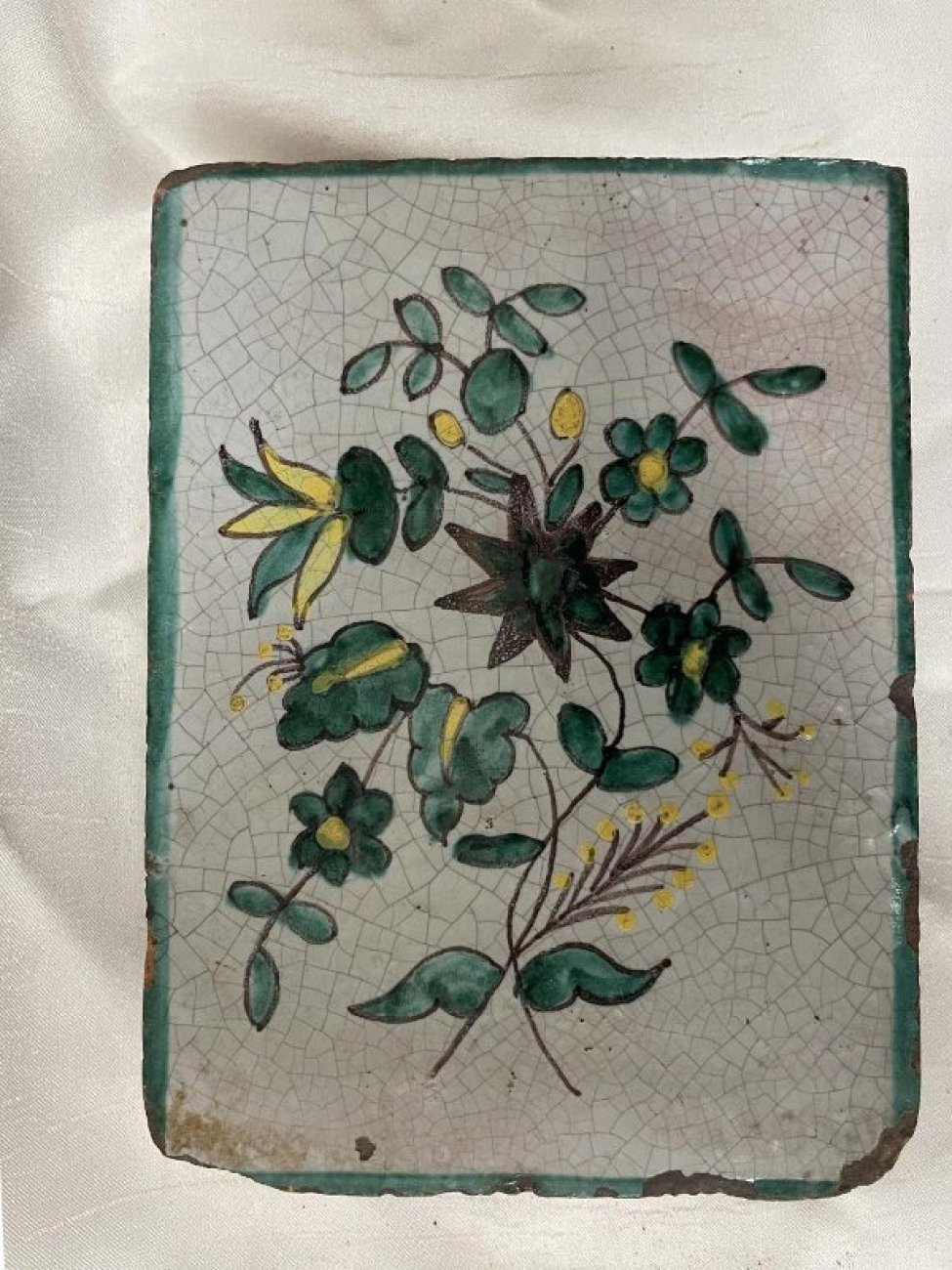 Изразец с изображением цветов и колосьев, сделанных коричневым и зелёным цветом на белом фоне.